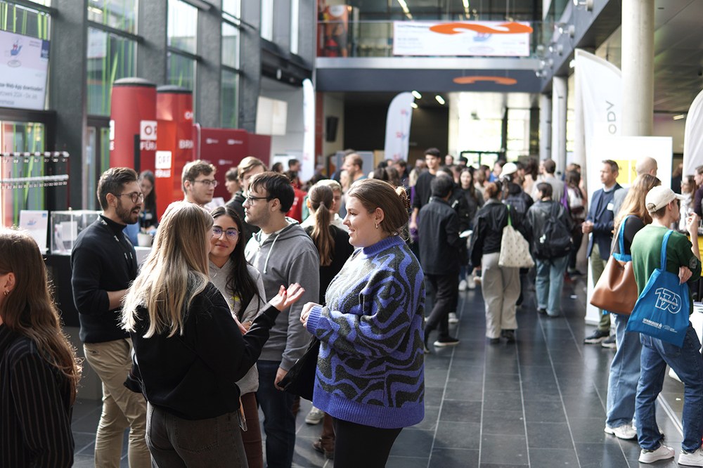 Belebte Messeszene in einem modernen Gebäude: Zahlreiche Personen stehen in Gruppen, führen Gespräche und informieren sich an Ständen. Im Hintergrund Banner und Infotafeln, die eine karriere.netzwerk-Veranstaltung kennzeichnen.