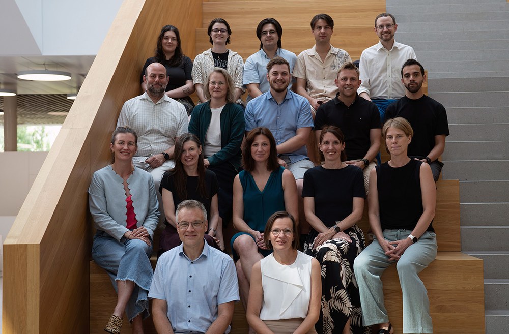 Gruppenfoto des Kollegiums der USTP 2026 vor dem Campusgebäude. Die Kollegiumsmitglieder stehen im Freien auf einem Weg vor dem Eingangsbereich der Hochschule.