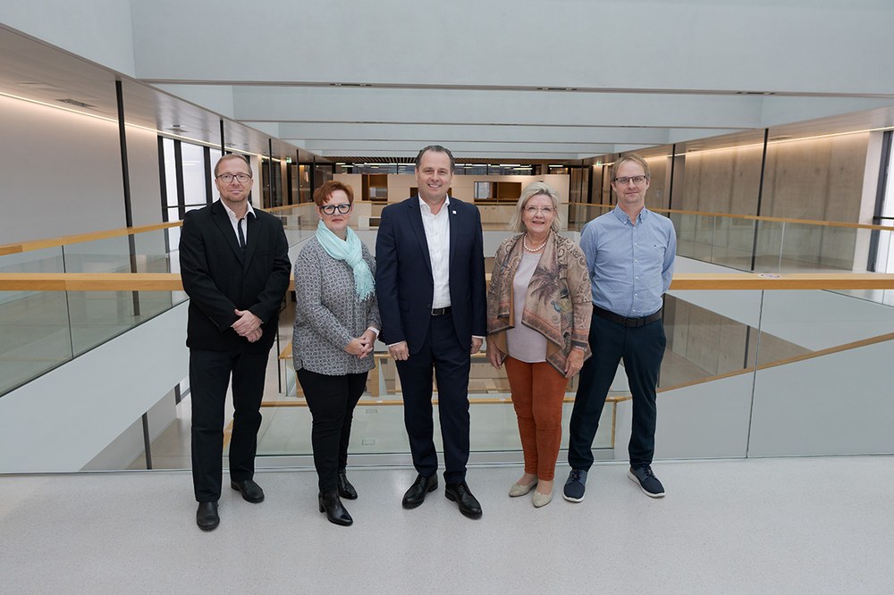 Five members of the supervisory board stand side by side in the modern, light-filled building of Campus St. Pölten. Glass railings and wooden details are visible in the background. All individuals are looking directly at the camera.