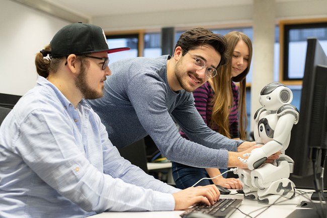 Sudierende im Data Science Lab vor einem Computerbildschirm mit einem Roboter