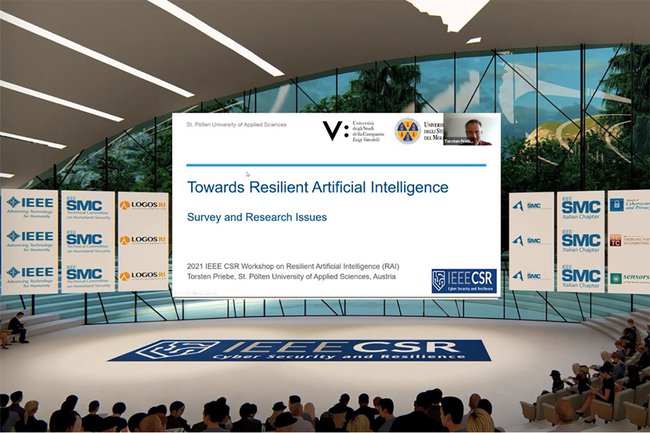 Hörsaal: Im Vordergrund sitzen Leute, vorne ist eine große Leindwand, auf der die Präsentation läuft