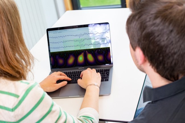 A man and a woman sitting in front of a laptop - on the screen there are EEG monitoring data